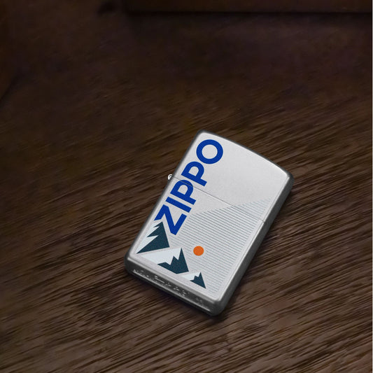 Lifestyle image of Zippo Mountain Design Satin Chrome Windproof Lighter lying flat on a dark wooden table showing the front of the lighter. 

