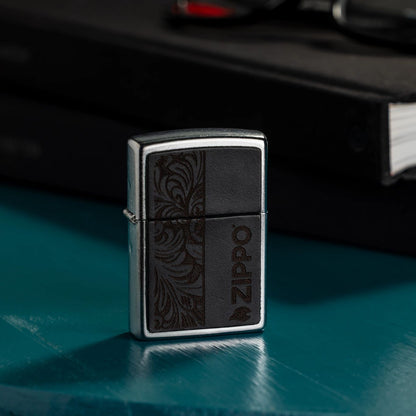 Lifestyle image of Zippo Black Leather Emblem - Zippo Design Street Chrome Windproof Lighter standing on a desk next to books and a pair of eyeglasses.