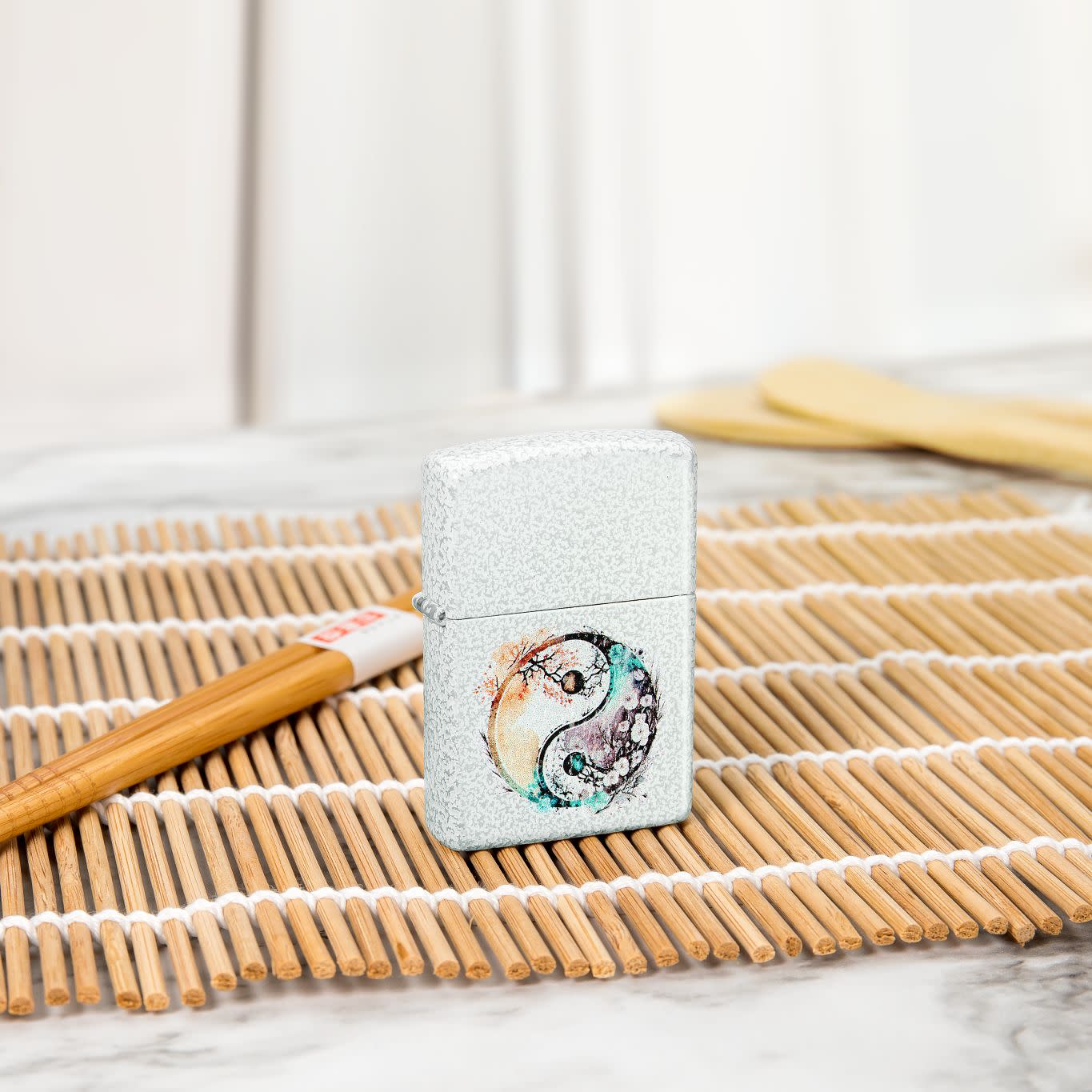 Lifestyle image of Zippo Floral Yin and Yang Design Glacier Windproof Lighter standing on a wooden placemat with chopsticks nearby.