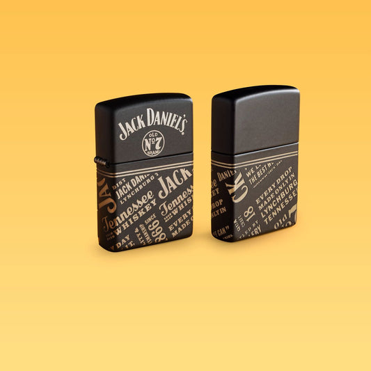 Lifestyle image of two Zippo Jack Daniel'sÂ® Every Drop Design Regular Media Chrome Black Matte Windproof Lighters standing with a pale yellow background.