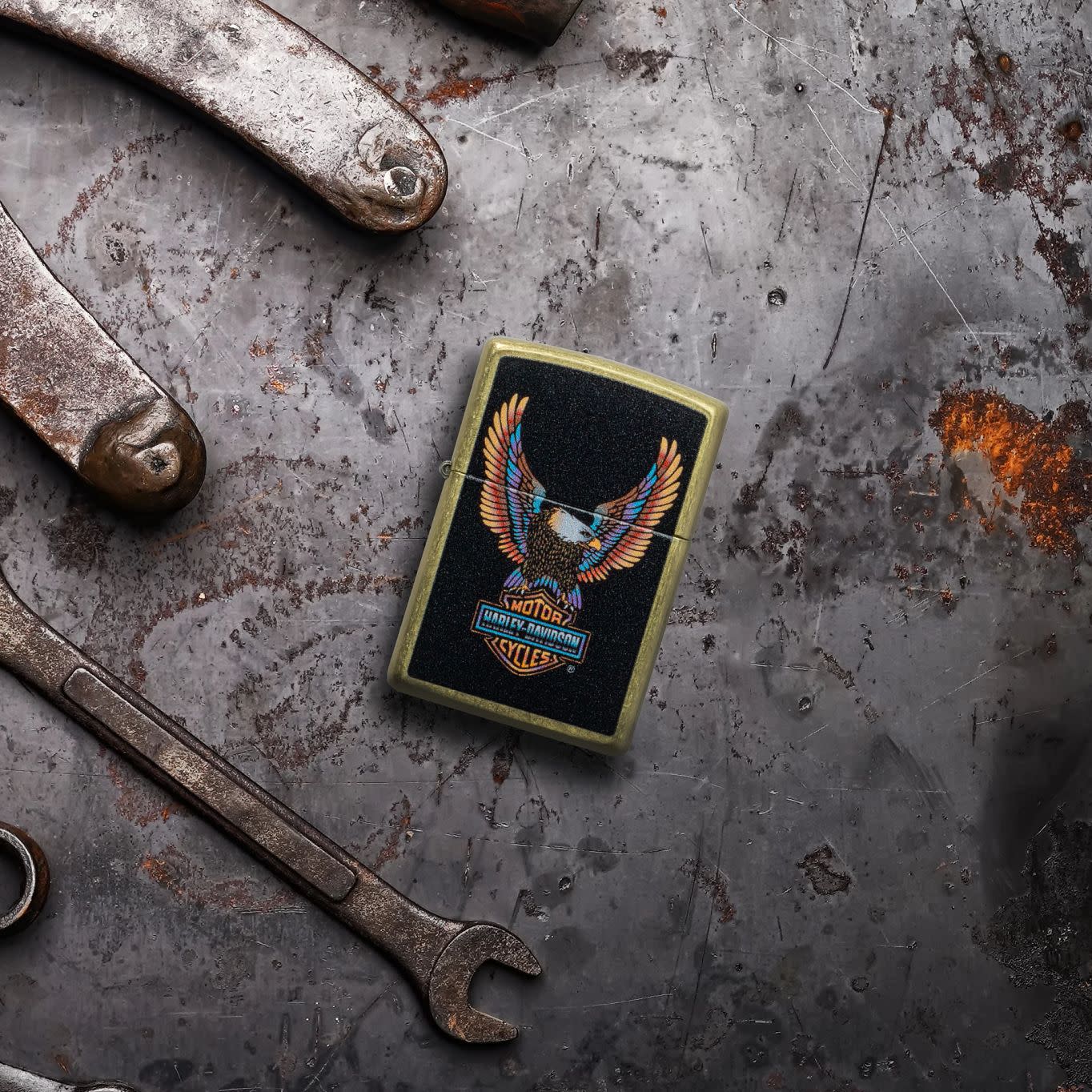 Lifestyle image of Zippo Harley-DavidsonÂ® Eagle Street Brass Windproof Lighter laying on a rusted and dented piece of metal with tools surrounding it.